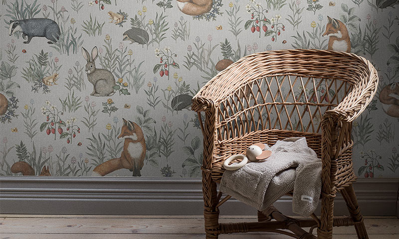 Grå barneromstapet med skogsdyr, rottingstol med beige pledd og babytreleke