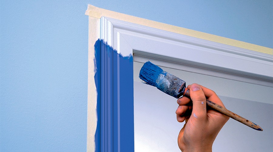 Hånd med pensel maler hvit dørkarm blå mot lys blå vegg.