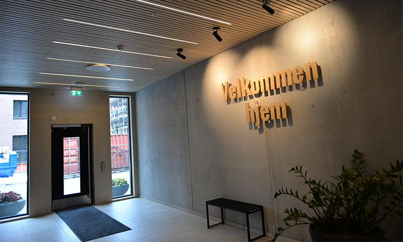 Moderne inngangsparti med betongvegg, “Velkommen hjem”-skilt, benk og plante.