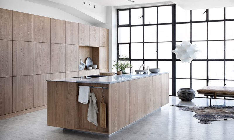 Lyst, moderne kjøkken med eikekledde skap, grå marmortopp og store svarte vindusrammer.