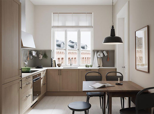 Lyst kjøkken med lyse treskap, grå benkeplate, vindu mot murstein, svart pendellampe og trebord.