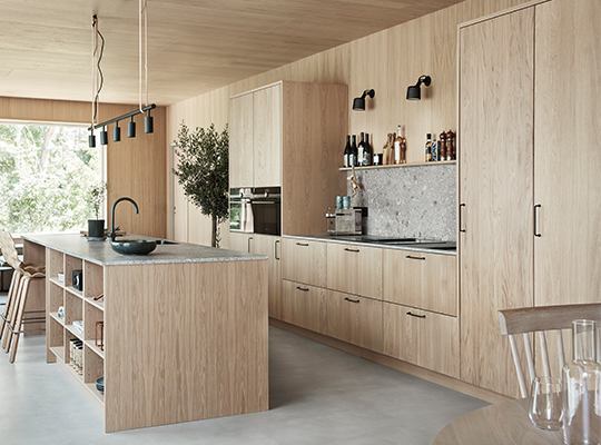 Lyst trekjøkken med kjøkkenøy i grå stein, sorte armaturer, flasker på hylle og grønn plante