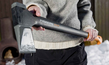 Person i grå genser holder svart-oransje Fiskars-øks foran snødekt bakgrunn.