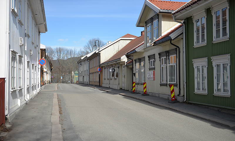 Tom småbygate med hvite, beige og grønne trehus og røde tak under blå himmel