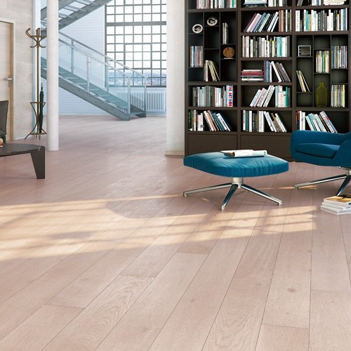 Lyst åpent rom med eikegulv, mørk bokhylle, blå lenestol og puff, metalltrapp ved store vinduer