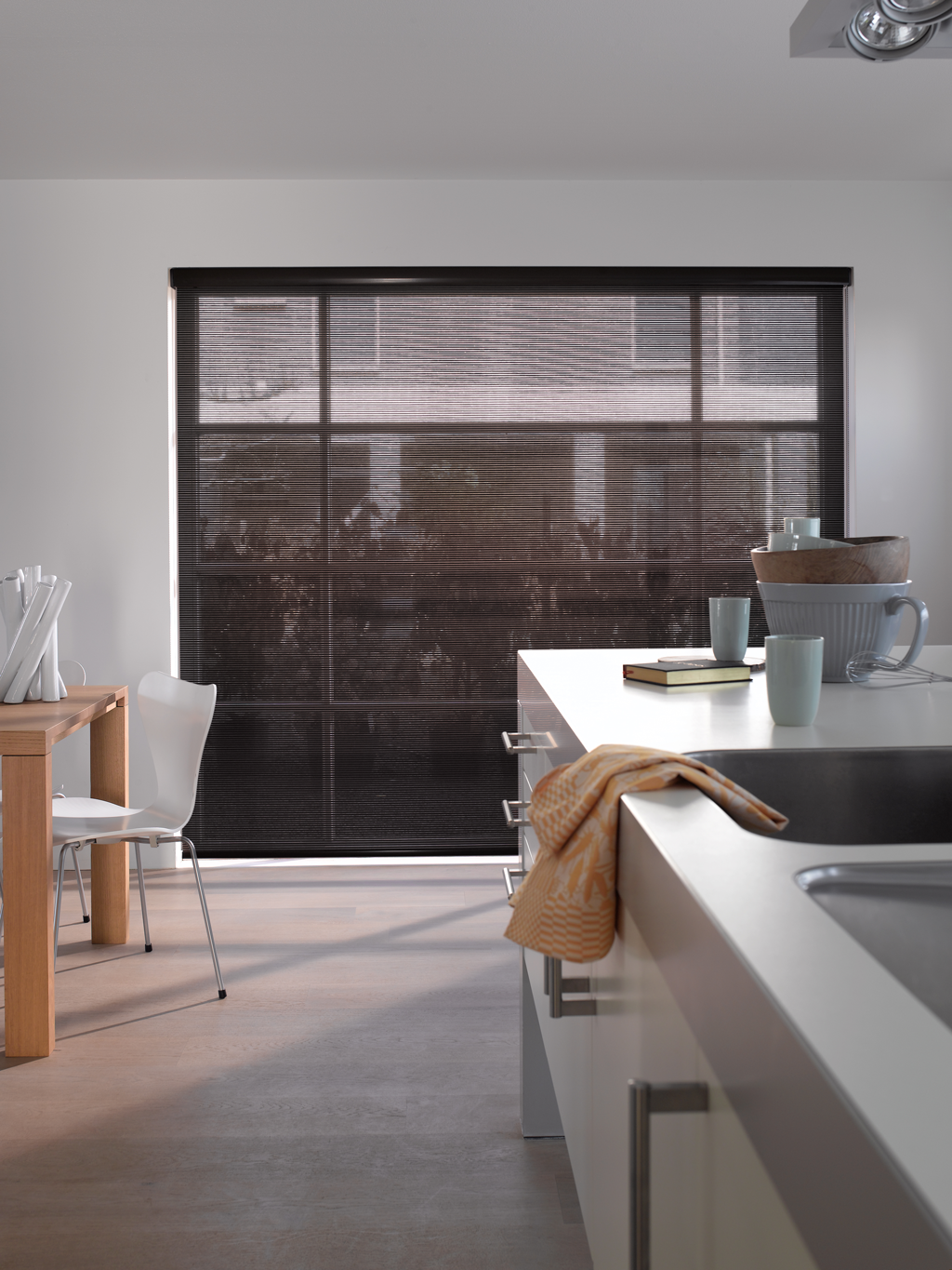 Moderne kjøkken med hvit benkeøy, svart rullegardin, trebord og oransje kjøkkenhåndkle.