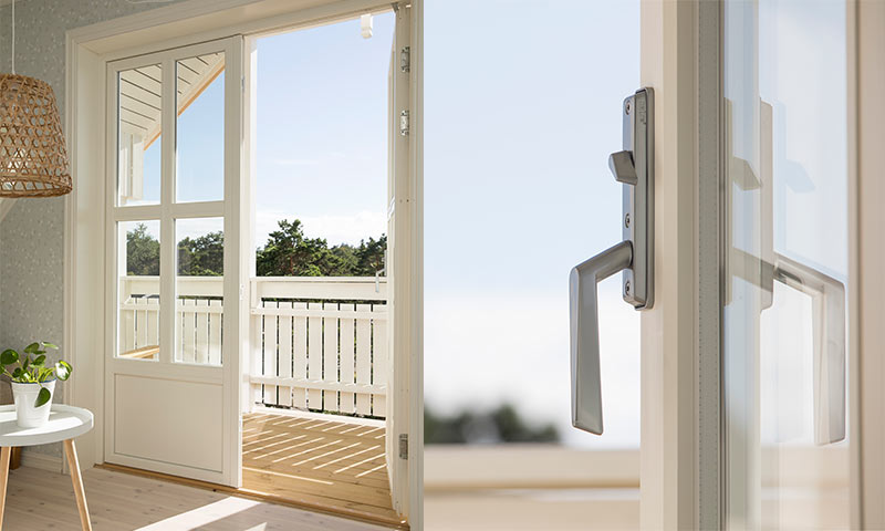 Åpen hvit glassdør mot solfylt tregulvbalkong med hvitt rekkverk og grønn skog i bakgrunnen