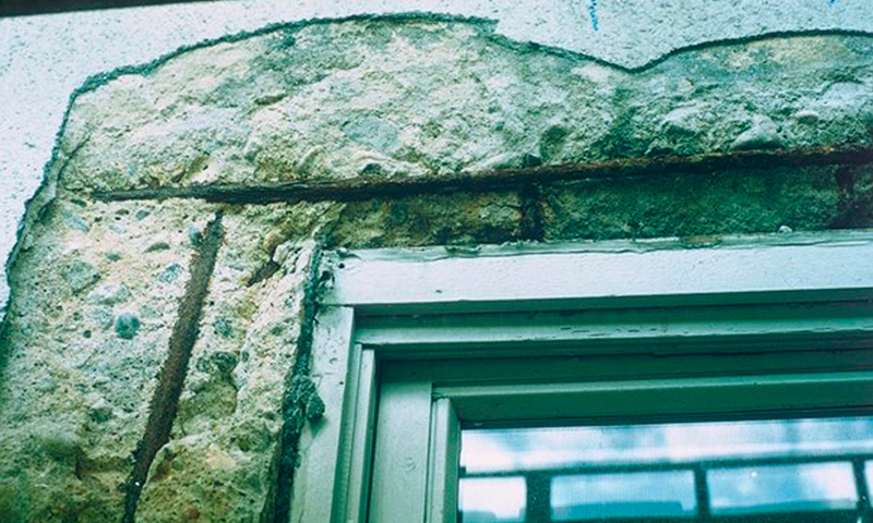 Slitt sandfarget betongvegg med rustent armeringsjern og hvit-grønn vindusramme