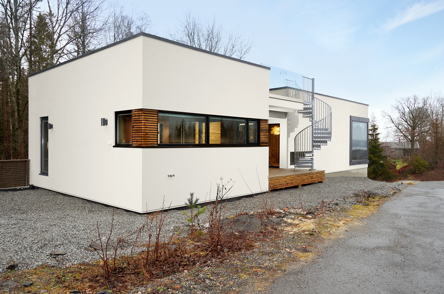 Moderne hvitt funkishus med trekledning, spiraltrapp til takterrasse og grusgang i skogsbryn