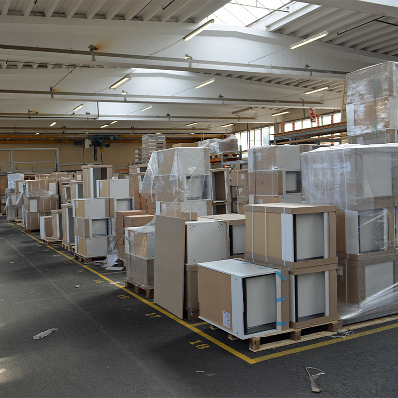 Lagerhall med brune kartonger og hvite møbelkasser innpakket i plast på paller