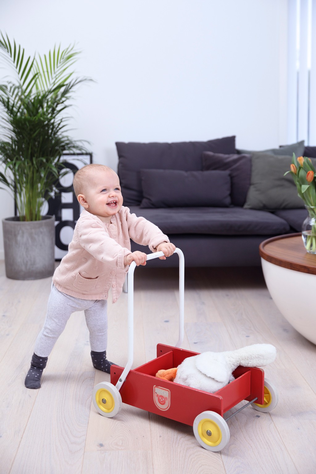 Lite barn i rosa genser dytter rød lekkevogn med kosekanin i lys, moderne stue