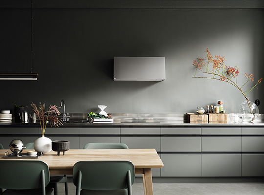 Minimalistisk kjøkken med grågrønne skap, stålbenk, trebord med grønne stoler, vase med blomster