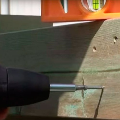 Svart drill driver skrue i værbitt grønn treplate med oransje vater på toppen.