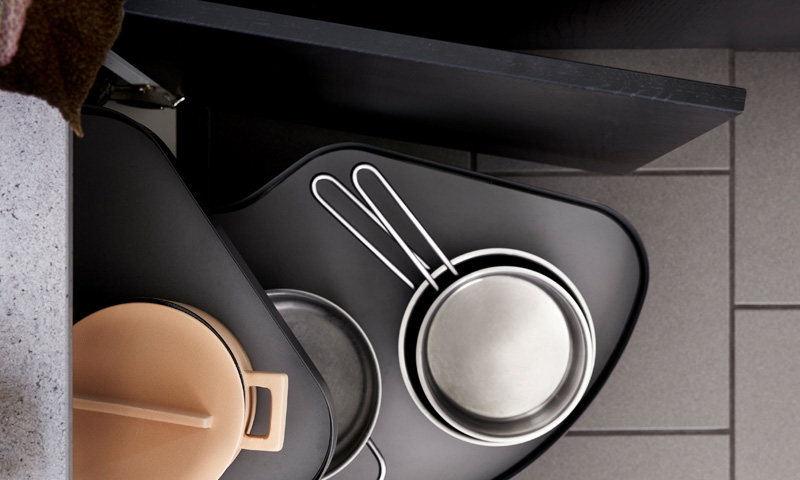 Åpnet kjøkkenskuff med svart uttrekkshylle, beige gryte med lokk og to stålpanner med hvite håndtak