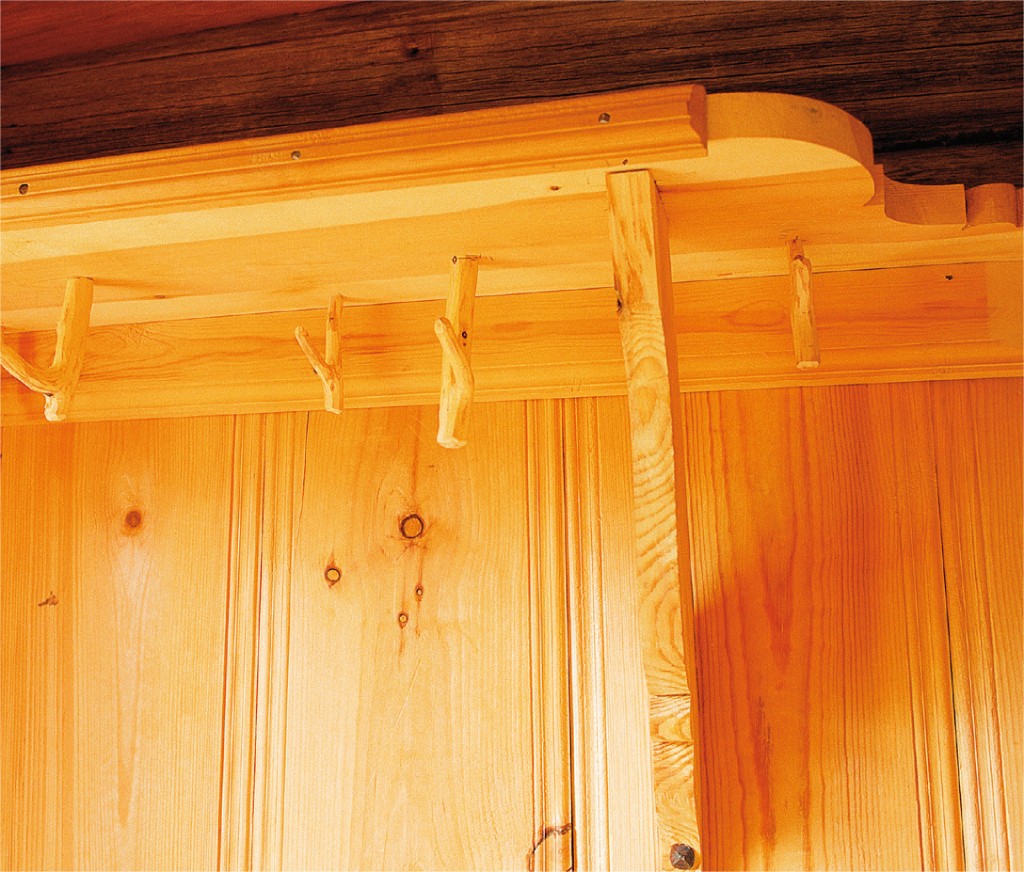 Rustikk oransje beiset trehylle med fire kvistkroker mot panelvegg