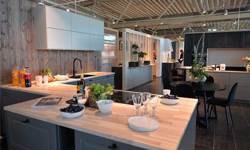 Moderne kjøkkenutstilling med grå skap, lys tref benkeplate, svart armatur og dekor