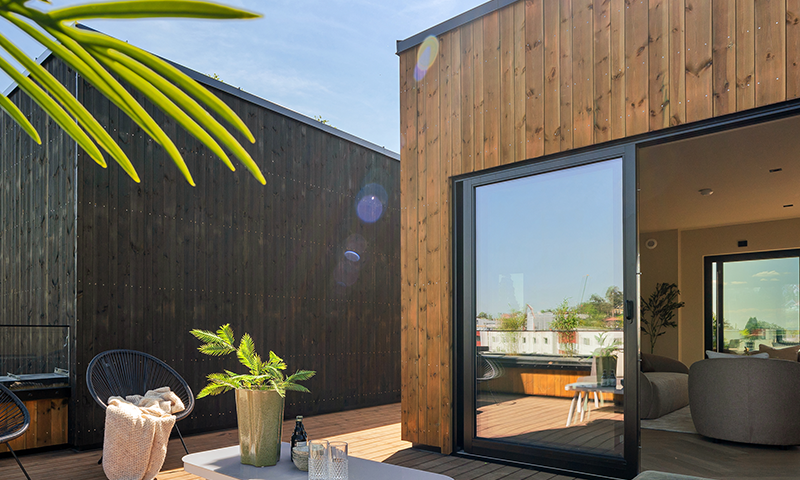 Moderne uteplass med sorte vinduer og lys brun kledning