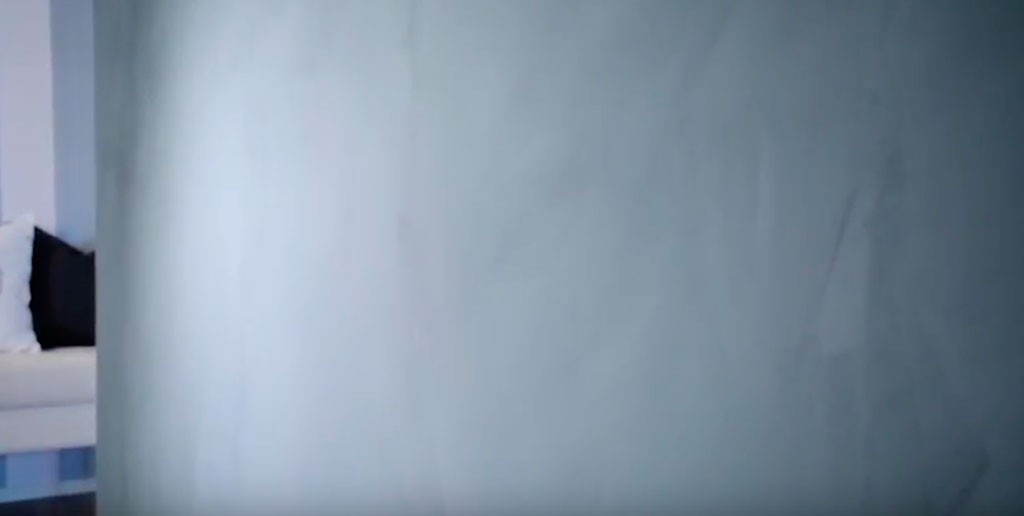 Ugjennomsiktig lyseblå glassvegg foran hvit sofa med svart pute i lyst oppholdsrom