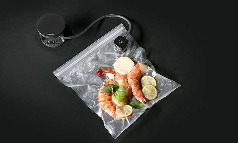 To rosa reker med lime, hvitløk og basilikum vakuumpakket i plastpose ved svart sous vide-maskin.