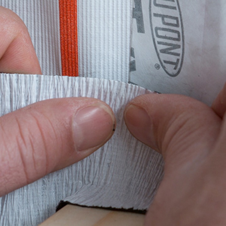 To hender trykker grått tetningsbånd mot DuPont-byggmembran med rødt strekk