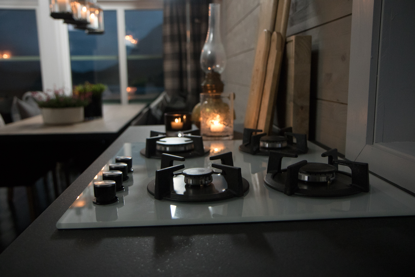 Hvitt glasskomfyr med fire svarte gassbrennere, tent oljelampe og tre skjærefjøler bak