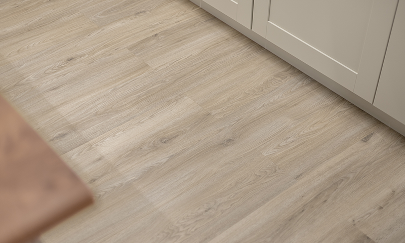 Nærbilde av lyst eikegulv ved kremfargede kjøkkenskap og bordkant