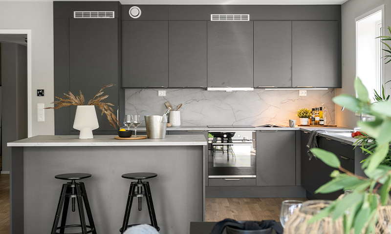 Moderne grått kjøkken med kjøkkenøy, to svarte barkrakker, marmorfliser, planter og glass