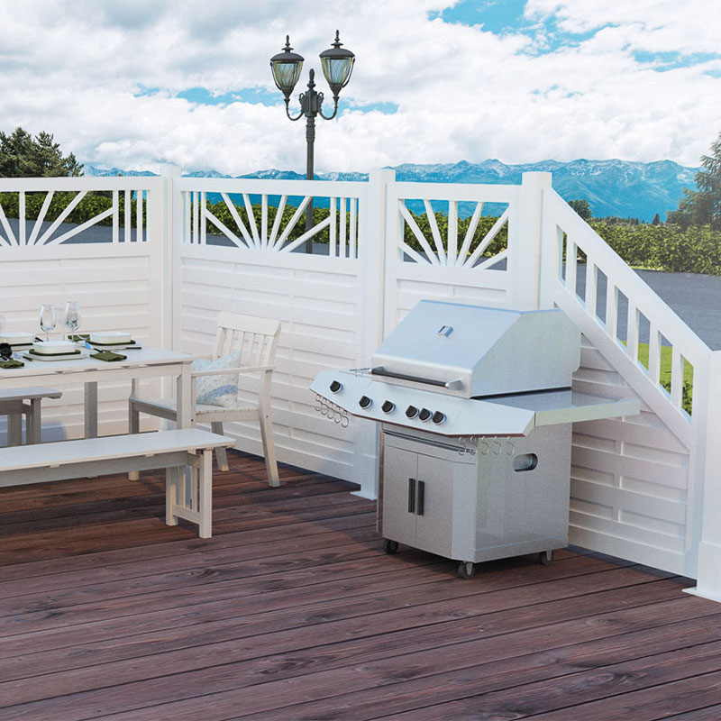 Hvit panelgjerde, stålgrill og hvitt hagebord med glass på mørkt tredekke, fjell bak.