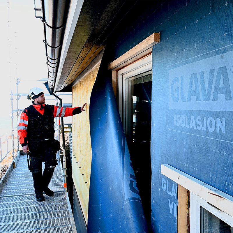 Arbeider på stillas fester blå Glava-isolasjonsduk over gul isolasjon på husfasade.