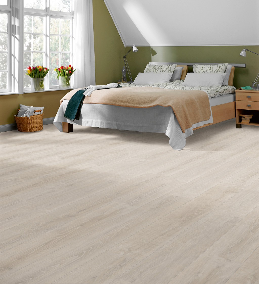 Loftsoverom med stor vindusflate, lys eikegulv, olivengrønn vegg, seng med beige teppe og tulipaner.