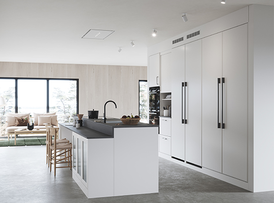 Moderne lyst kjøkken med hvite skap, svart benkeplate, tre barstoler og sofa ved vindu