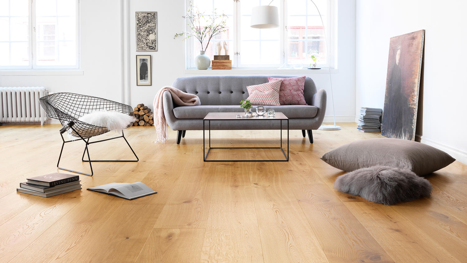 Lys stue med grå sofa, rosa puter, svart trådstol, lavt glassbord og eikegulv.