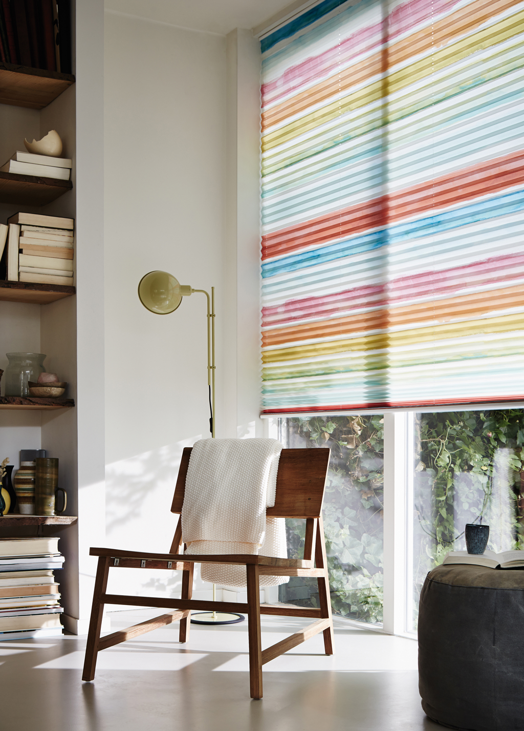 Lyst lesekrok med trestol og hvitt pledd foran fargerik stripete rullegardin og gulvlampe.