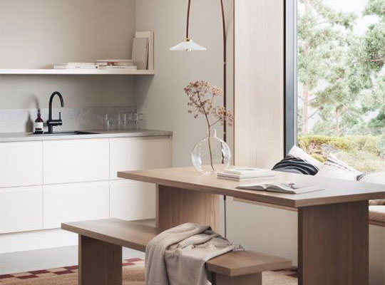 Moderne lyst kjøkken med hvite skap, svart kran, trebord med benk, glassvase, lampe og hageutsikt