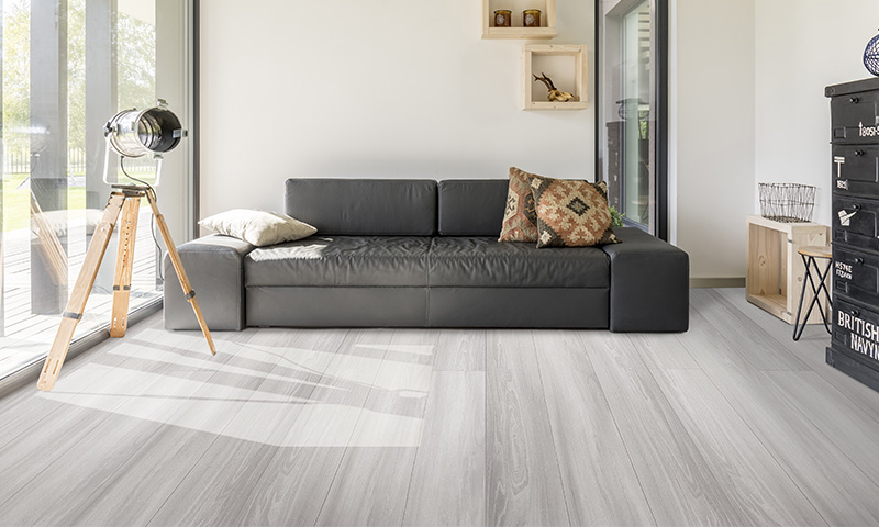 Lyst, minimalistisk stue med sort skinnsofa, mønstret pute, trebent gulvlampe og lyst tregulv