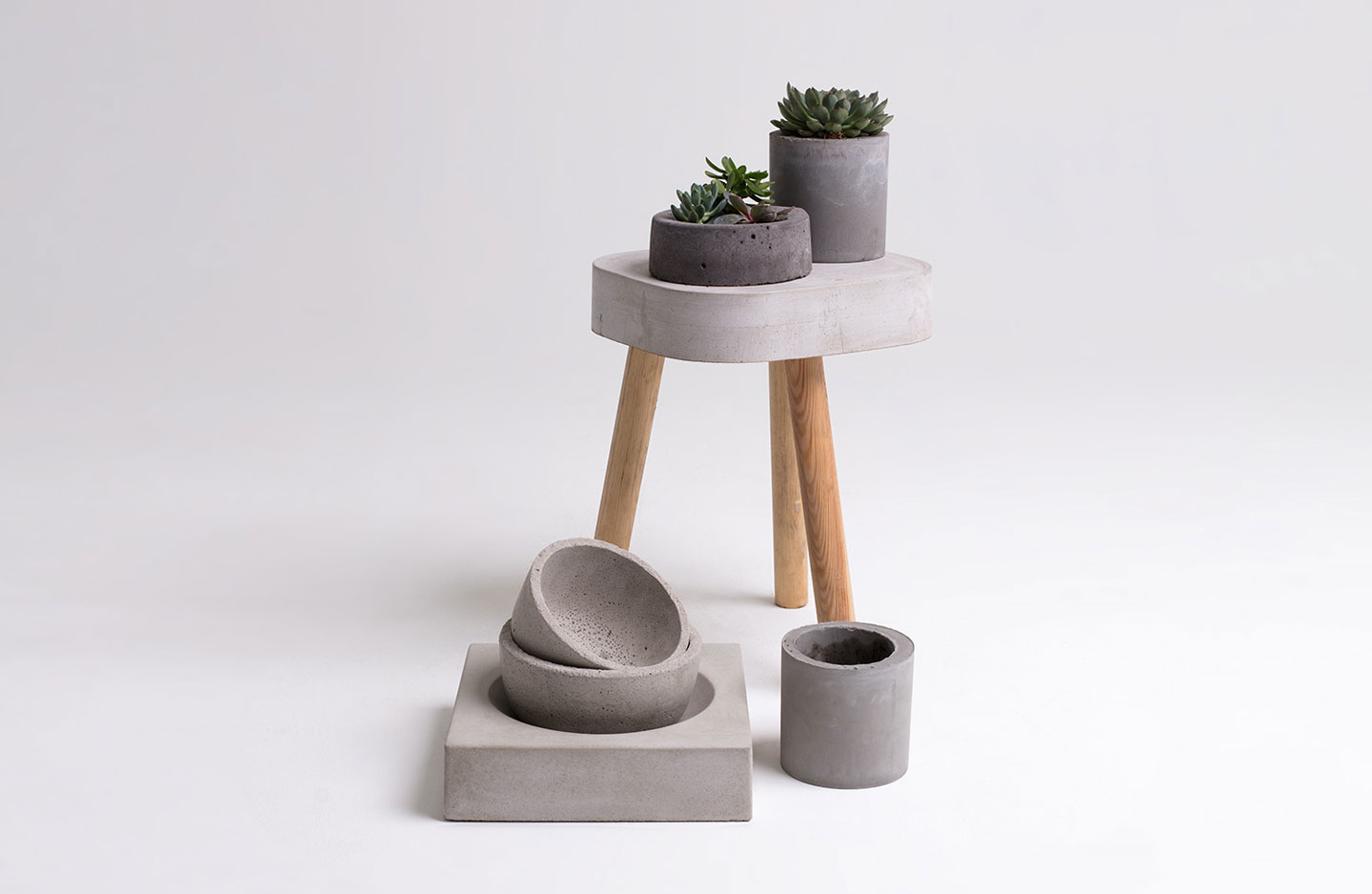 Minimalistisk oppstilling med grå betongpotter med sukkulenter på hvit bakgrunn