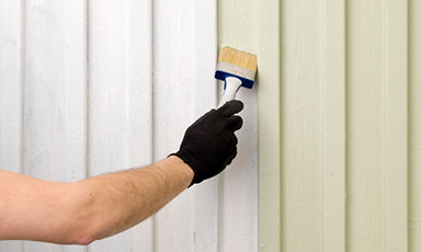 En hånd med svart hanske maler en vegg med en pensel, fra hvit til lysegrønn farge.