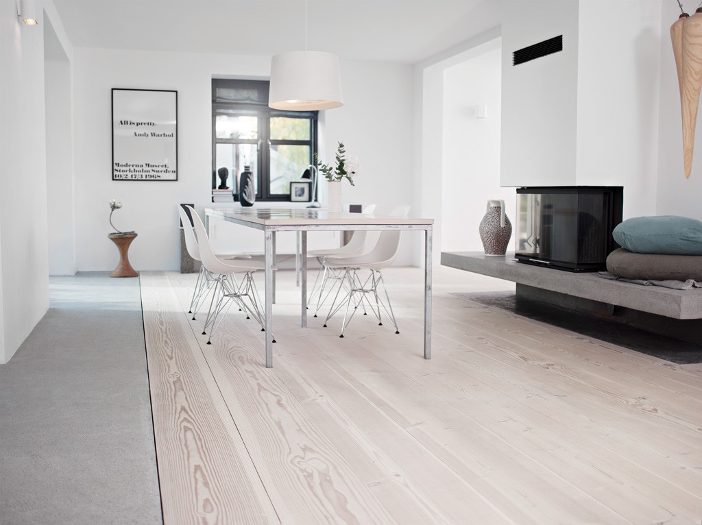 Lyst, minimalistisk rom med hvitt metallspisebord, fire hvite stoler, lyst tregulv og peis.