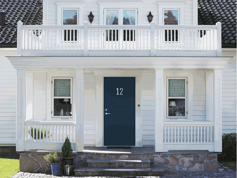 Hvit to-etasjes hus med veranda og balkong, mørk blå dør nr 12, steintrapp og potteplanter.