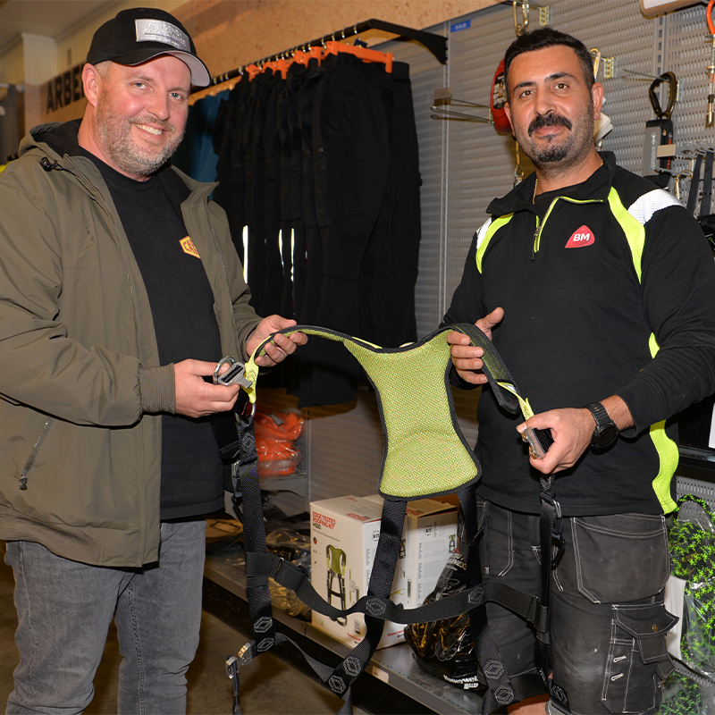 To menn holder grønt arbeidssele i byggevarebutikk omgitt av verneutstyr