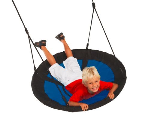 Blond gutt i rød T-skjorte og hvite shorts ligger på blå-svart rund gunga.