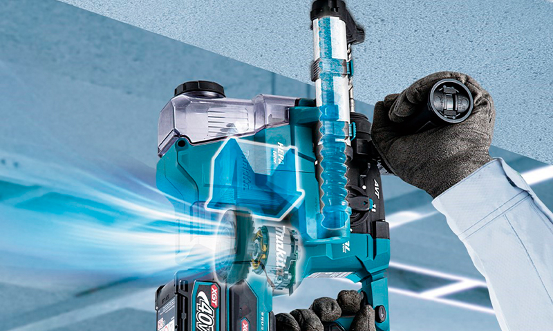 Hånd i hanske holder turkis borhammer med støvavsug mot lyseblått tak, blå luftstrømmer.