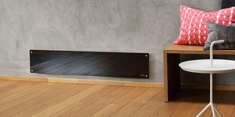 Svart glasspanelovn på grå vegg over lyst tregulv, ved trebenk med rosa puter og hvitt bord