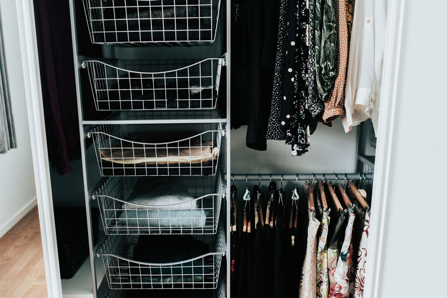 Åpen garderobe med hvite metallkurver med brettede gensere og hengende mønstrede klær.