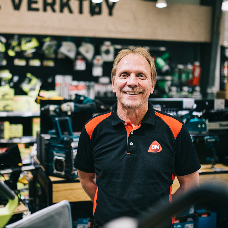 Ansatt i svart-oransje BM-polo foran verktøyhylle i lys jernvarebutikk