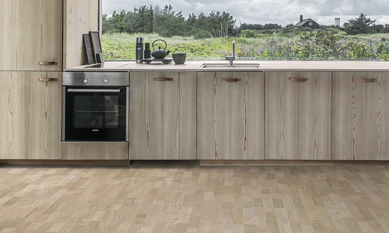 Lyst trekjøkken med integrert ovn, vask og tekanne foran vindu mot grønn eng.