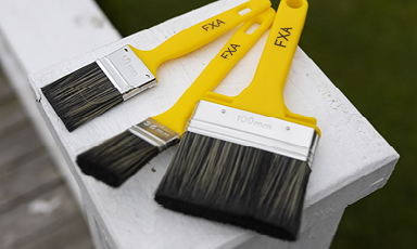 Tre gule malerkoster med svarte børster på hvit malt rekkverk.