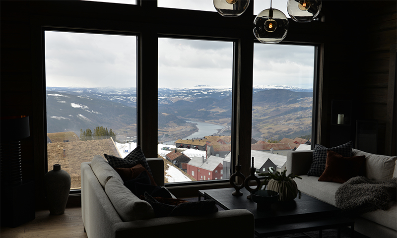 Stue med lyse sofaer og panoramautsikt til snødekte fjell, dal og innsjø.