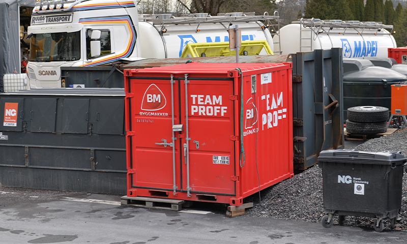 Rød Team Proff-container på byggeplass foran hvit Scania-lastebil og svarte avfallsbeholdere