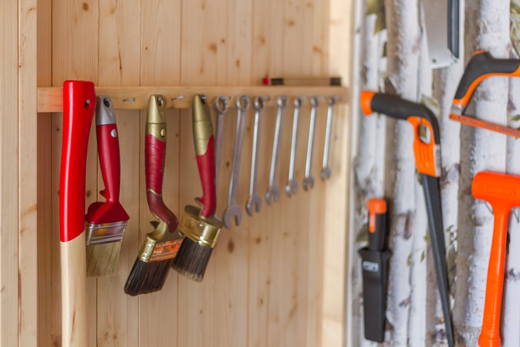 Røde malepensler, sølvfargede skiftenøkler og oransje verktøy på lys trevegg.